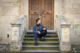Portrait of a young man sitting against a beautiful old medieval cathedral door. A man in front of