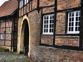 A close-up of a half-timbered house with brick walls and white windows, next to an archway, asbeck,