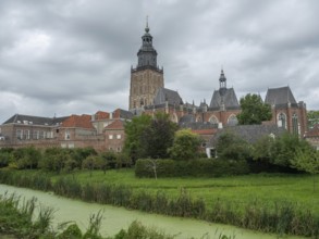 A medieval church with a high tower, surrounded by historic buildings and green countryside under a