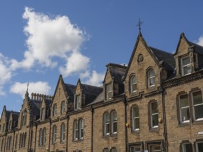 Row of historic buildings with pointed gables and stone facades under a blue sky in a cityscape,