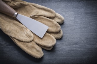 Single paint scraper on working glove and wooden board