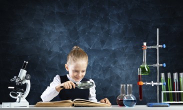 Little girl sitting at desk with magnifier and open book. Research and education in school. Happy
