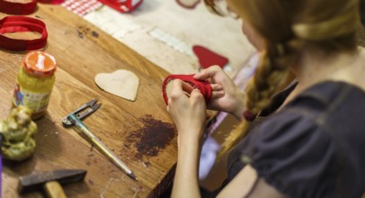 Brown-haired woman manufacturing heart-shaped red purses on the wooden table