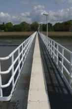 A long jetty stretches straight across the water, flanked by white railings under a blue sky,