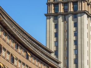 Modern building with a striking facade and a skyscraper in the background under a clear blue sky,