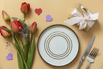 Beautiful table setting with gift box, decorative hearts and tulips flowers on pastel peach