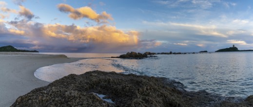 A panorama view of a colorful sunset at Nora Beach in Sardinia with the Coltellazzo Tower in the