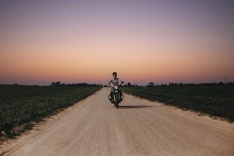 Rider on a motorcycle advances along a rural road during sunset, creating a serene atmosphere