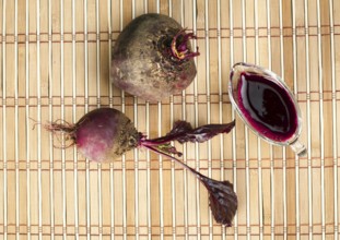 Red beets with leaves and jug with juice on wooden base