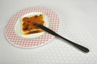 Spread jam on bread with knife. Pink checkered plate