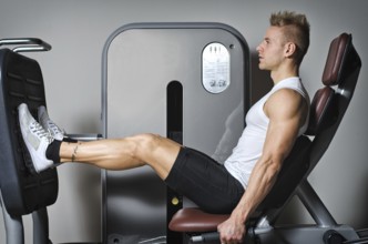 Attractive and fit young man in gym working out legs and exercising on equipment