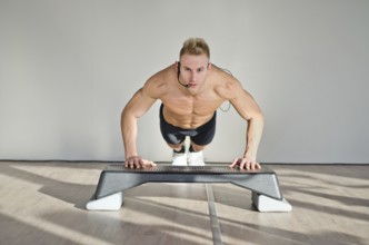 Young aerobics male coach shirtless leaning on step teaching class