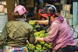 Two woman trading green fruits on Krong motorbikes in an urban environment, woman selling fruits in