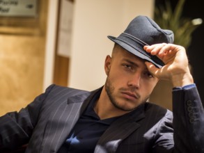 Handsome elegant man in hotel or night club lounge, wearing business suit and fedora hat, looking