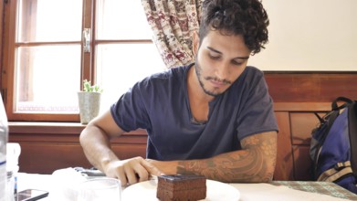Attractive young man in restaurant eating chocolate cake