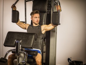 Muscular young man, training pecs on gym cable machine