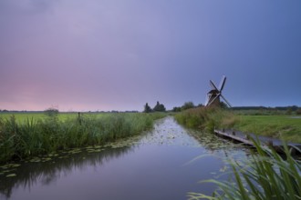 Charming windmill by river at rainy sunrise, Holland