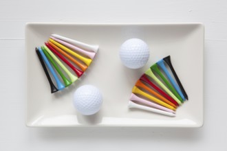 White ceramic dishes with golf balls and wooden tees on over white background, rectangle dish