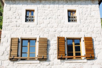 The house is white brick with large windows and wooden shutters below and small windows with metal