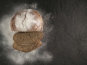 Sliced homemade sourdough rye bread with rye flour on black textured background. Top view or
