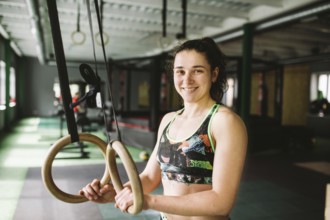 Beautiful girl doing an exercise on the gym rings in the gym. Happy and smiling