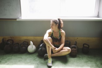 The girl is resting, taking a break during training in the gym. Sits by the window near a lot of