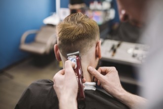 Close up shot of a man getting a trendy haircut at a hair salon. Male caucasian hairdresser serving