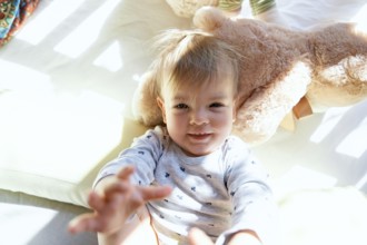 Small child lies in a wooden crib on a large teddy bear.