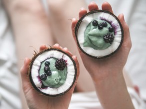 Two coconut half with smoothie or yogurt in woman hands. Blue spirulina smoothie in coconut with