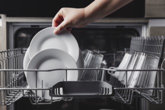 Female hand loading dished, empty out or unloading dishwasher with utensils. Kitchen appliances,