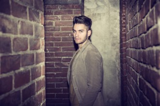Attractive young man standing against brick wall, looking at camera