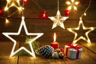 A candlelit wooden table with gifts, pine cones, and star lights
