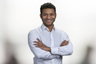 Handsome smiling man with crossed arms looking at camera. Portrait of indian businessman on blurred