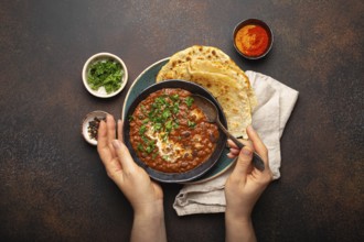 Female hands holding a bowl and eating traditional Indian Punjabi dish Dal makhani with lentils and