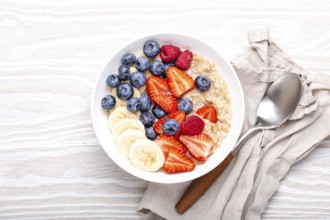 Oatmeal porridge with fruit and berries in bowl with spoon on white wooden background table top