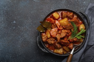 Beef meat stew with potatoes, carrot and delicious gravy in black casserole pot with bay leaves and