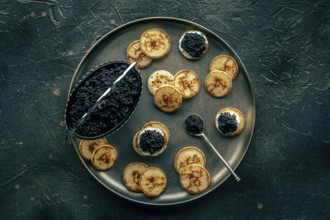 Blinis with black caviar and cream cheese, overhead flat lay shot on a black background, mini