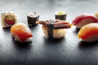 Sushi on a black slate plate. Nigiri with eel, salmon and tuna, roll with avocado and maki with
