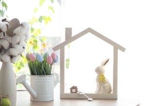 Key and tiny house of cozy home with Easter decor with rabbit and eggs on table of kitchen.
