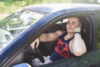 Portrait of smiling young man sitting in a car and looking at the camera on a sunny day