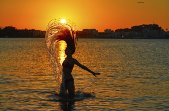 Girl flipping hair flip at sunset beach in orange sky