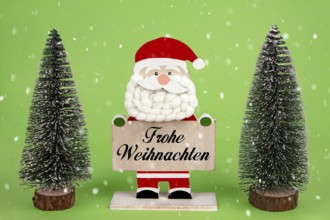 Dekorative hölzerne Santa Clause hält eine Tafel mit deutschem Text -Frohe Weihnachten- bedeutet