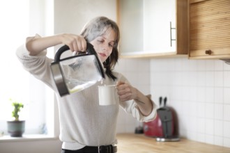 Woman pouring water into a cup in a bright kitchen with kettle, energy-saving, environmentally