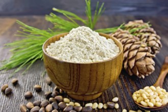 Flour cedar in a wooden bowl, cedar nuts and two cones, a spoon with peeled nuts, cedar branch