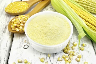 Flour corn in a bowl, groats and grain maize in the spoons, cobs on the background of wooden boards