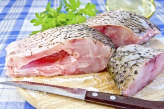 Bream raw sliced pieces on a circular board, parsley, vegetable oil, knife on blue linen tablecloth