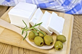 White brine cheese, rosemary, olive in spoon, blue plaid napkin on a wooden boards background