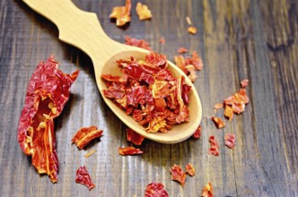 Red pepper flakes in a wooden spoon and a pod of dry red pepper on a wooden board