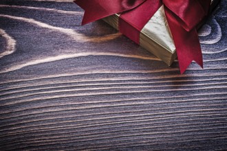 Present box with red satin ribbon on wooden board
