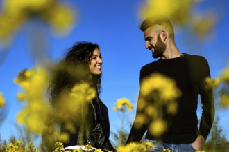 Portrait of a happy couple smiling holding hands looking at each other in a field of flowers in